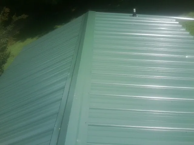 New green metal panels meeting at the ridge of a roof — Flat Roof Repair work by our crew in Allensville
