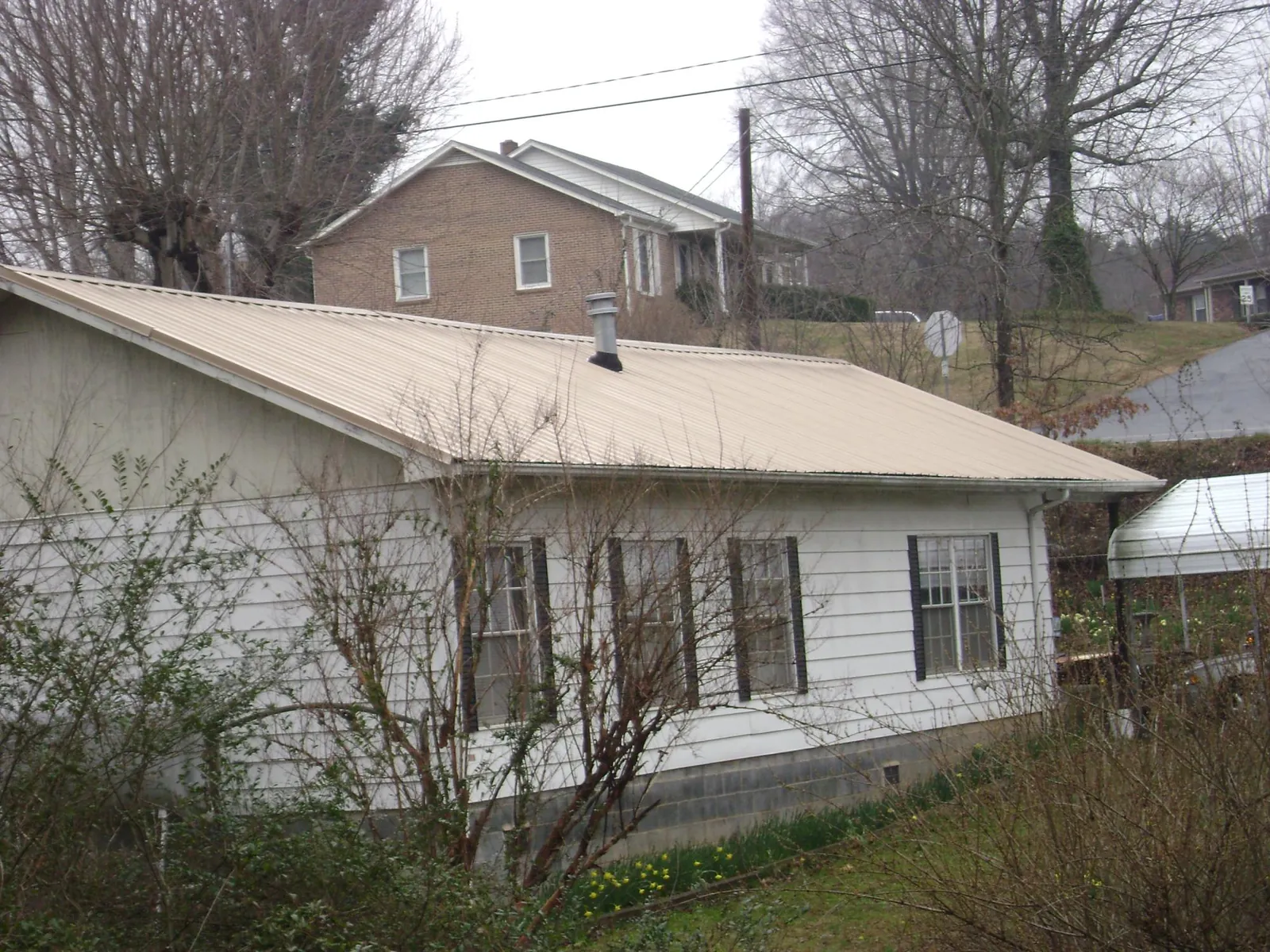 Tan metal roof on a white sided house set into a hillside — Commercial Roofing by Roofing Brothers in Allensville